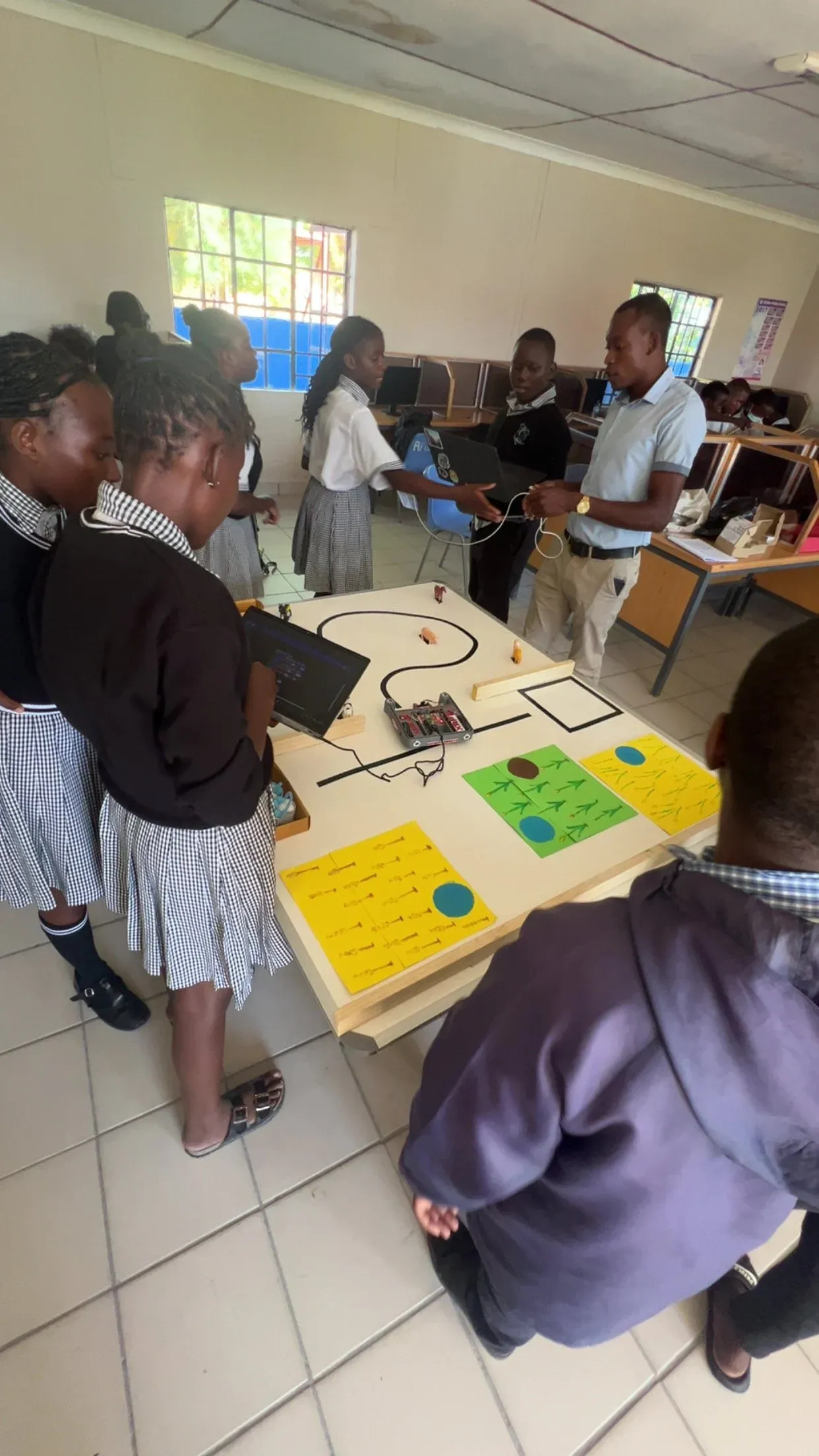 Namibian students gathering around a line-following robot on a classroom table